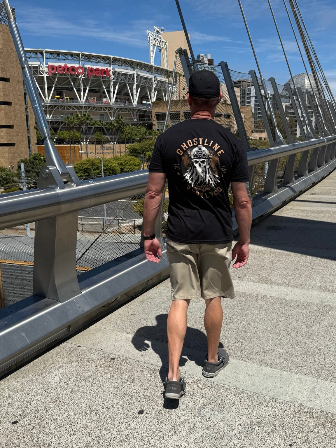 Back of a black Ghostline graphic tee worn on a pedestrian bridge