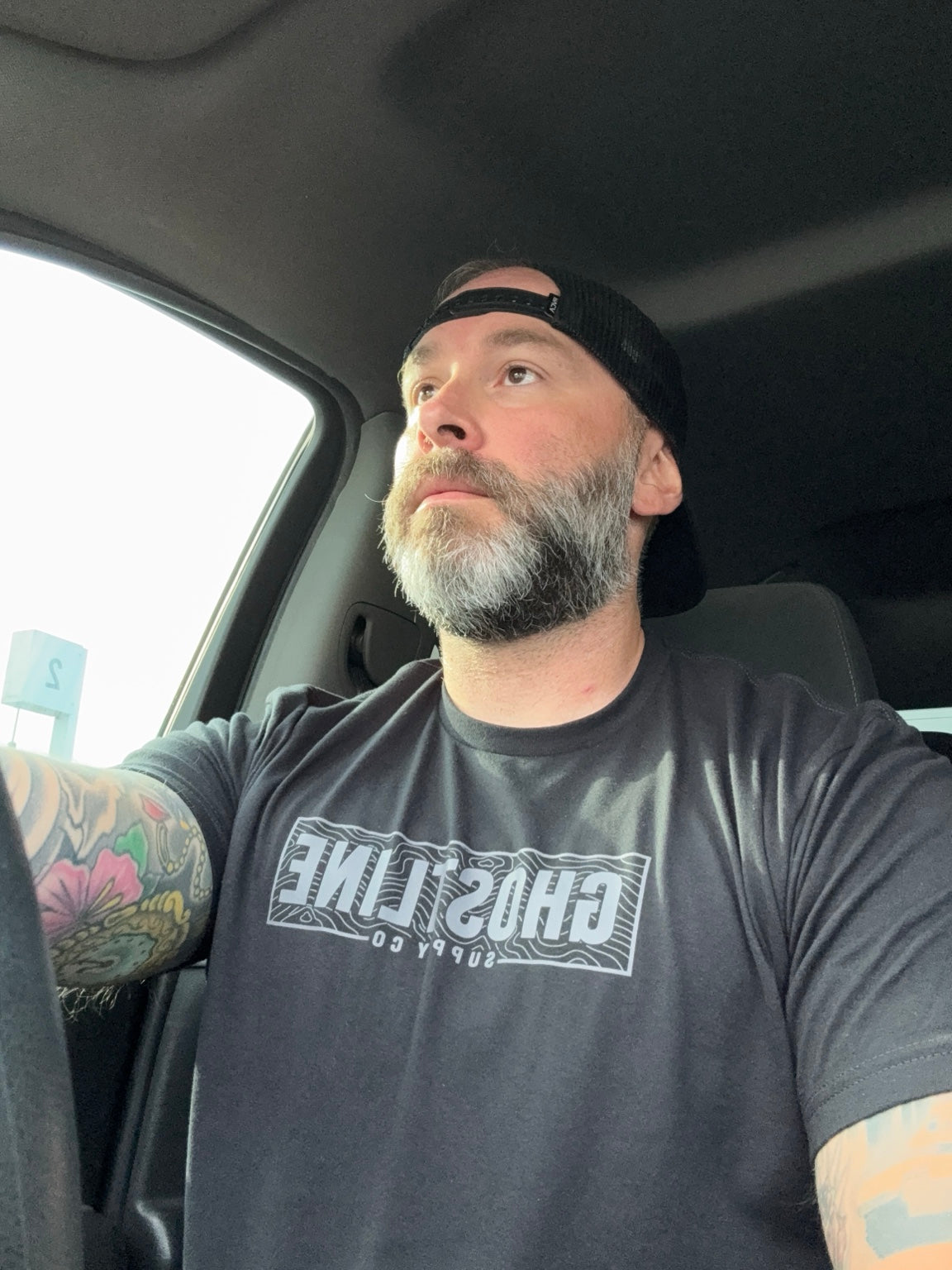 Ghostline Topo Tee worn in a vehicle, showing the chest graphic and athletic fit.